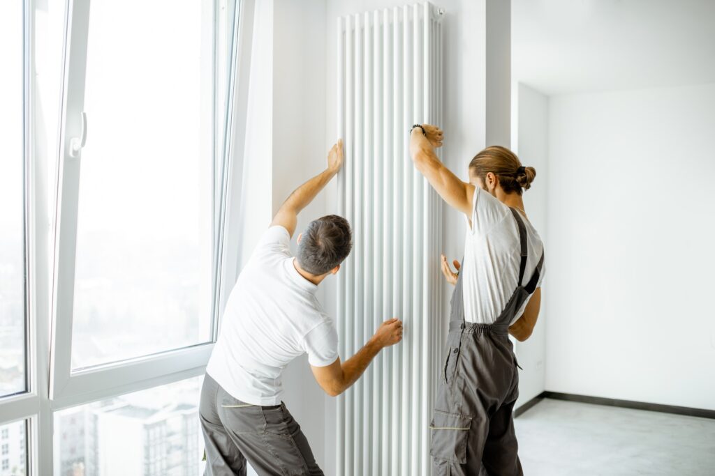Two men repairing a radiator in a room, focused on their task with tools and equipment nearby.